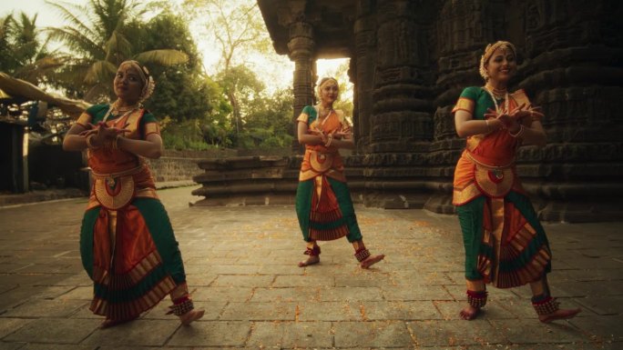 三位富有表现力的年轻印度舞者在古庙中表演民间舞蹈的慢动作肖像。穿着传统服装的妇女穿着五颜六色的纱丽跳