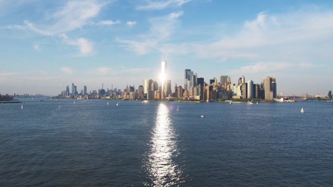 航拍镜头的摄像机接近曼哈顿岛的办公室和公寓大楼。哈德逊河风景与游艇，船只和太阳反射从一个世界贸易中心