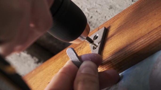用螺丝刀将衣服钩拧到墙上的木板上