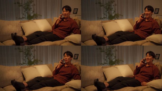 兴奋的韩国男子接听电话。晚上，英俊的亚洲男性舒适地坐在舒适客厅的沙发上，与朋友、家人或爱人聊天