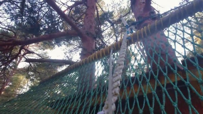 慢动作运动员带着安全绳在冒险公园的安全网上跳跃，爬网在树林里的树台上练习。冒险公园在立陶宛的极限运动