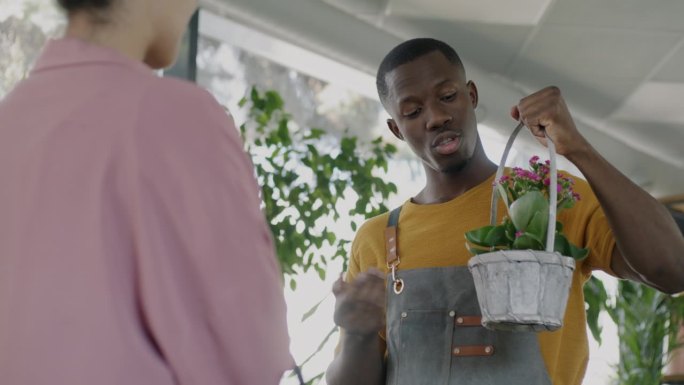 非裔美国男店员在花店向女顾客推销盛开的植物