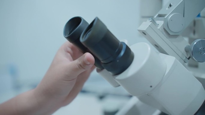 在扫描电子显微镜上，一位女科学家调整她眼睛的焦点来观察微小的细节。