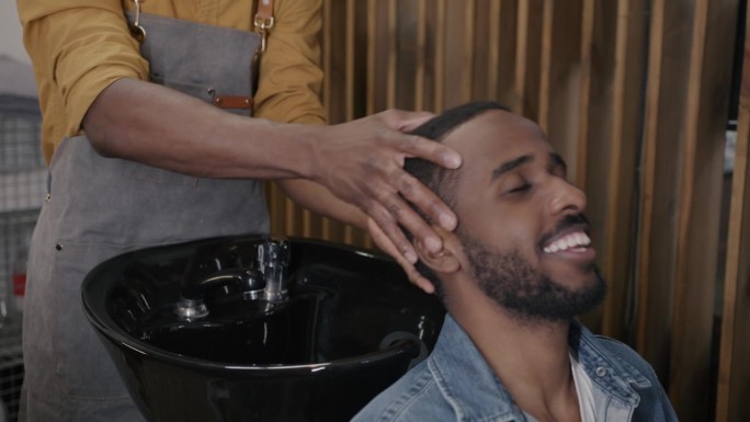 男理发师在理发店里准备给年轻的非裔美国人洗头