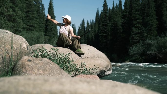 一位兴高采烈的女游客坐在山林的河上拍摄视频