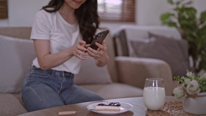 年轻漂亮的亚洲女性女士开心放松好玩用科技手机拍下美味的蛋糕甜点放在餐桌上的白色盘子上，现代社交网络习