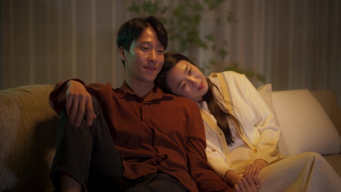 一对韩国夫妇在电视上观看浪漫喜剧电影的肖像。快乐的男朋友和女朋友一起在家享受有趣的电视连续剧，一起坐