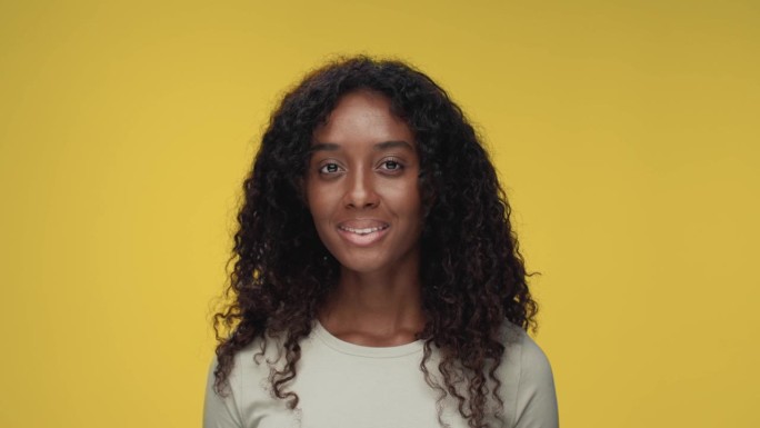 在彩色摄影工作室拍摄的年轻黑人妇女看着相机微笑的肖像。快乐开朗的女孩孤独的黄色背景特写。非裔美国人，