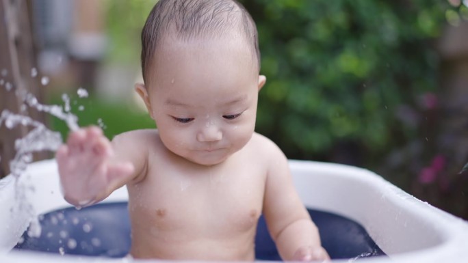 小男孩玩得很开心，把水溅到婴儿浴盆上。