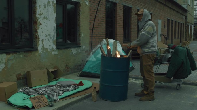 无家可归的人在火桶和他的庇护所附近暖手