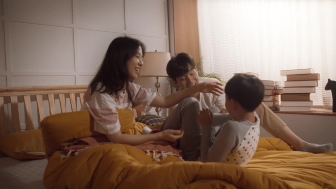 可爱的韩国家庭在早上:活跃和顽皮的孩子跑到他的父母的卧室叫醒他们。兴奋的男孩被爸爸妈妈挠痒痒。快乐的