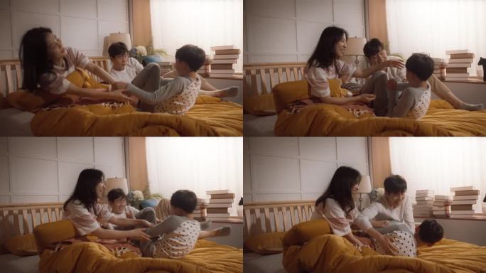 可爱的韩国家庭在早上:活跃和顽皮的孩子跑到他的父母的卧室叫醒他们。兴奋的男孩被爸爸妈妈挠痒痒。快乐的