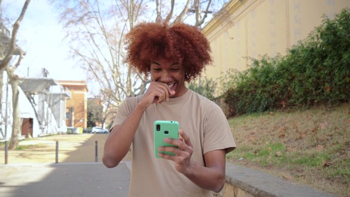 一个非裔美国青少年用手机发送有趣的信息。孤独快乐的年轻人微笑着玩智能手机。酷酷帅气的男学生用手机软件
