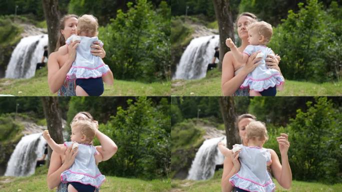在瀑布附近的大自然中，母亲和女婴坐在户外野餐毯上