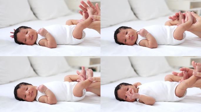 一个皮肤白皙的女人的妈妈的手轻轻地抚摸着一个刚出生的非洲裔美国婴儿的腿，一个刚睡醒或睡着的小孩躺在卧