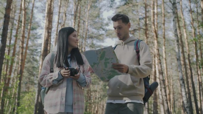 年轻的男人和女人走在森林里，看着地图，在夏天的一天探索区域