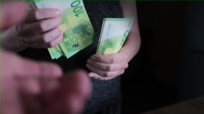 女人数着一捆欧元，把一部分钱交给一个伸出来的男人的手，近距离。