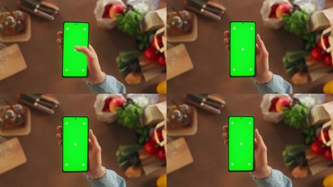 顶部静态视图匿名妇女使用智能手机与模拟绿色屏幕Chromakey显示在厨房餐桌上的食物配料。女性在流