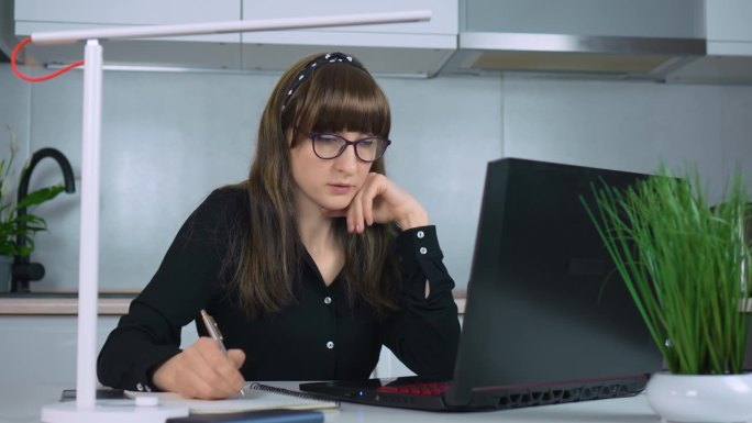 女商人在家庭办公室用笔记本电脑工作，而在工作场所用每日计划表做笔记