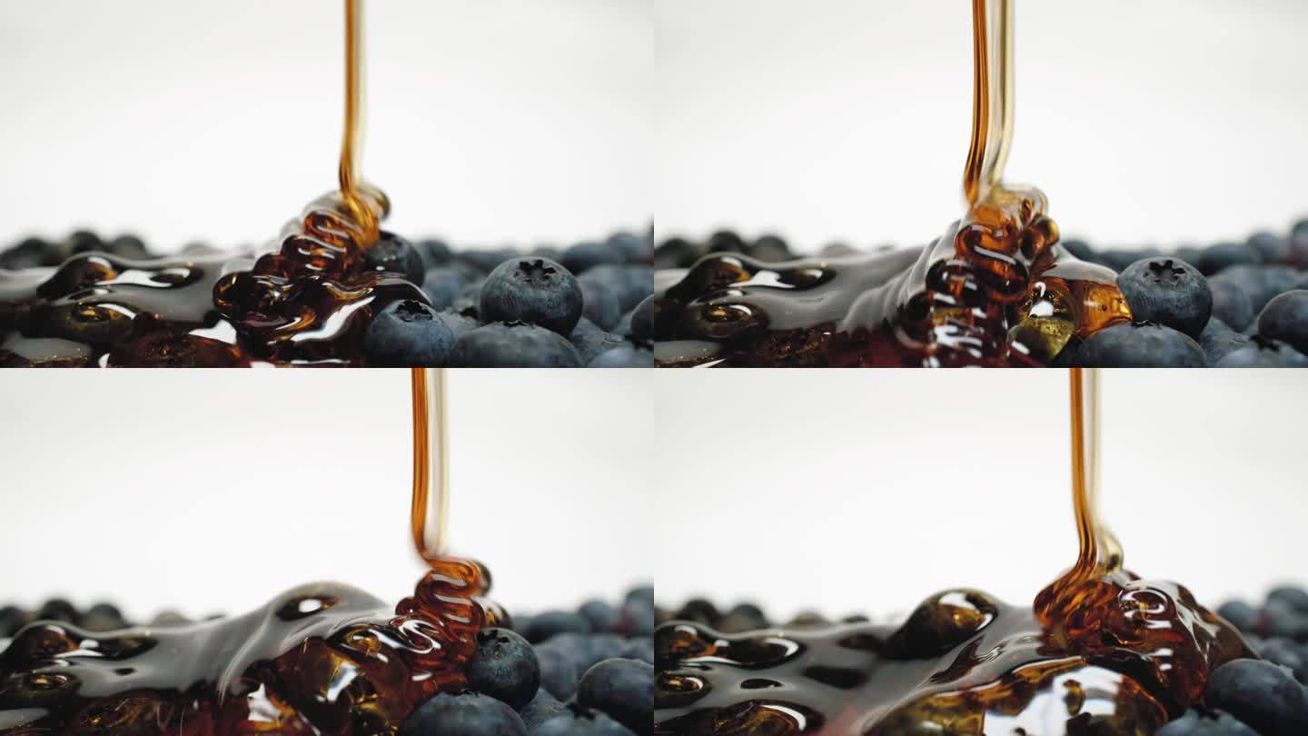 特写宏观蜂蜜倒在蓝莓上，成熟的有机新鲜浆果在白色背景上拍摄