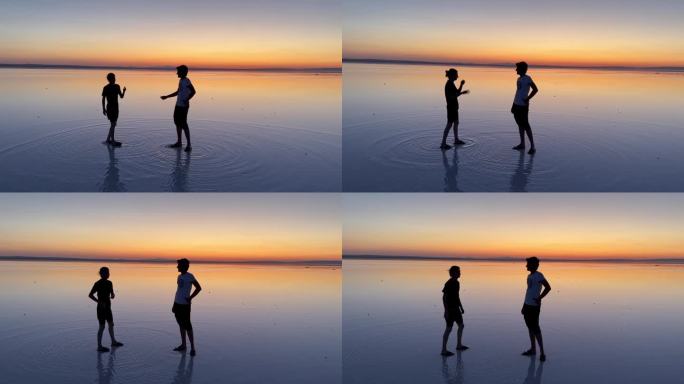 夕阳下，两个青春期的男孩站在盐湖的浅水区边说边握手