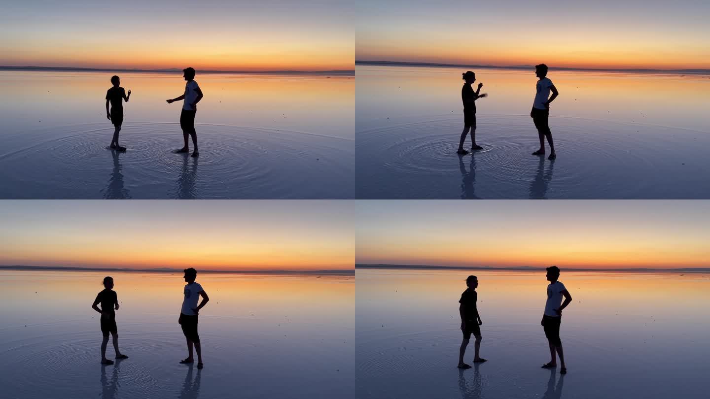 夕阳下，两个青春期的男孩站在盐湖的浅水区边说边握手