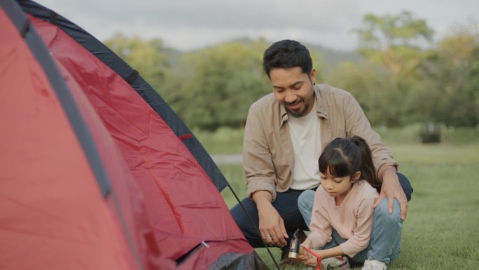 亚洲父亲和女儿在湖边露营，周末家庭度假活动。