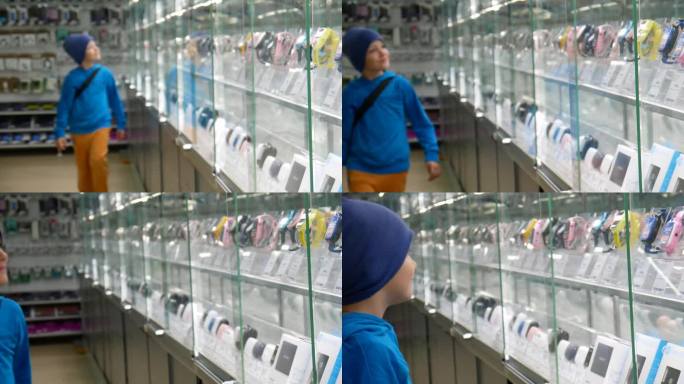 一个可爱的快乐男孩带着数码产品走过展示柜，仔细地检查着它们