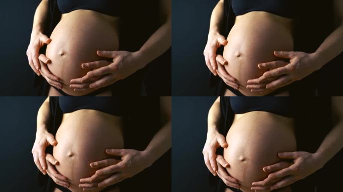 孕妈妈在父母的手牵着内衣跳舞的腹部特写。怀孕最后一个月，第36周。侧角视图。黑色背景。