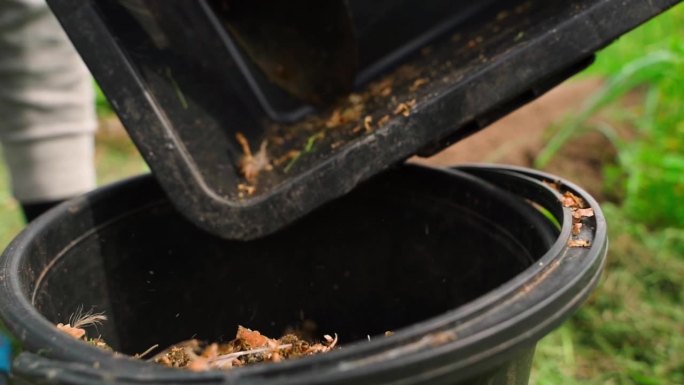 鸟粪和木屑被扔进一个黑色的塑料桶，特写