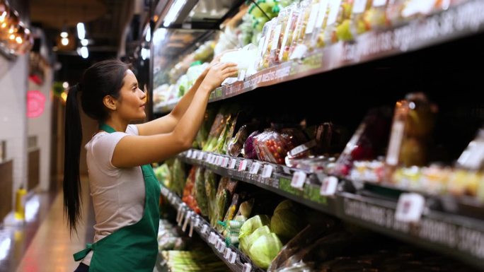 开朗美丽的女售货员在超市的冷藏区整理农产品