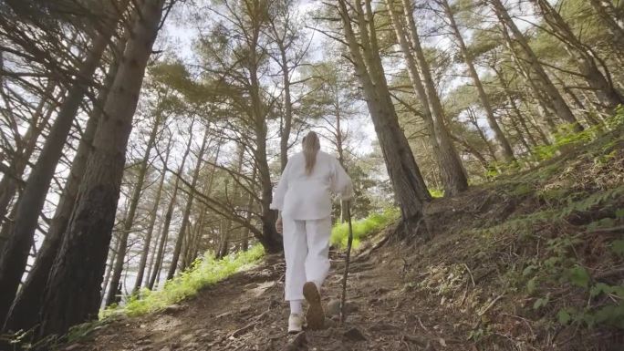穿白衣的女人手里拿着棍子在树林里散步