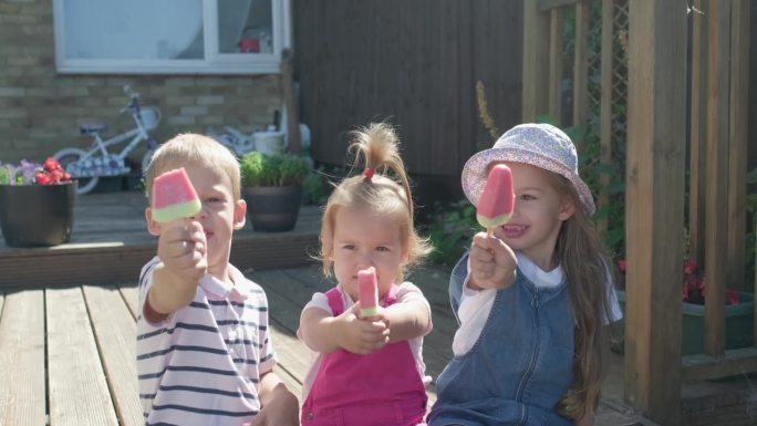 三个可爱的小孩在享用美味的甜筒冰淇淋。吃西瓜冰棒的孩子。孩子们兄弟姐妹们在家庭花园吃糖果。暑假炎热的