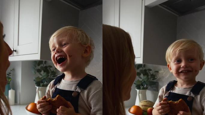 母亲和小儿子在家厨房吃大饼干的垂直视频