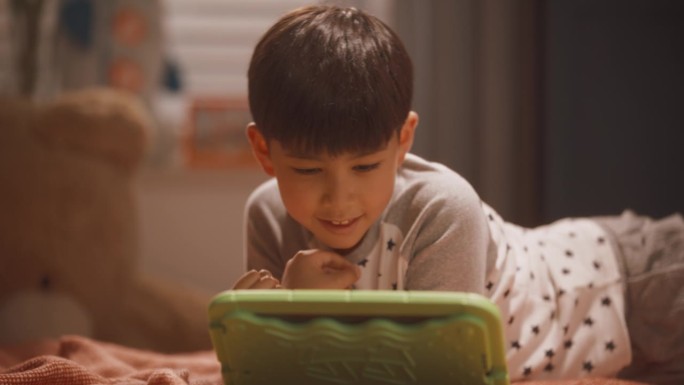 聪明的韩国男孩在孩子卧室的平板电脑上玩教育和学习游戏。快乐的孩子在赢得另一轮电子游戏后庆祝