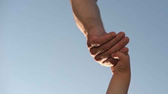 蓝天背景上，大人牵着小孩的手。父母伸出援手，帮助有需要的孩子。孩子们在握手。孩子的手伸向爸爸。家庭团