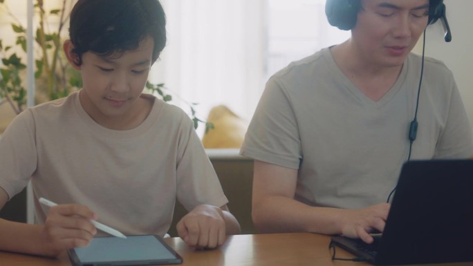 快乐的父亲和儿子在家里用笔记本电脑和平板电脑工作。