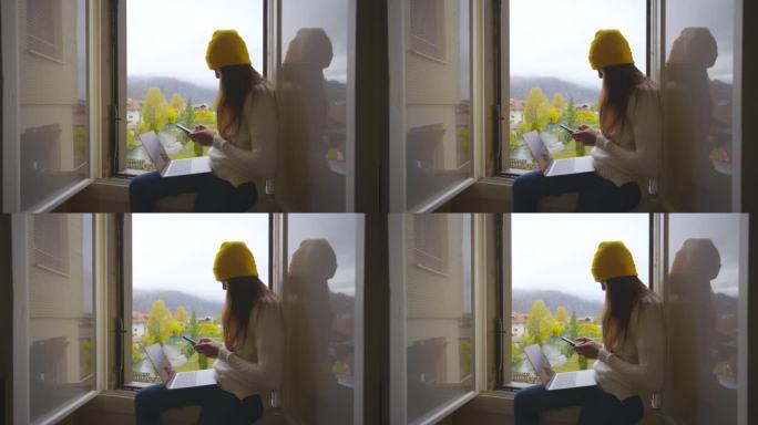 年轻女子坐在家里白色的窗台上玩智能手机。