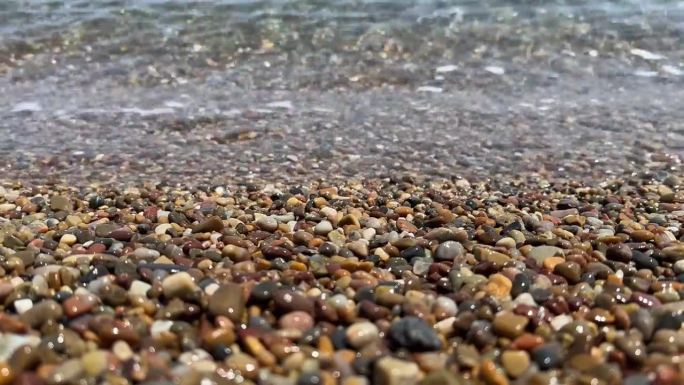 卵石滩的特写，透明的波浪和阳光照射在水面上。石质海岸的近景。自然背景的平静的大海在冲浪区