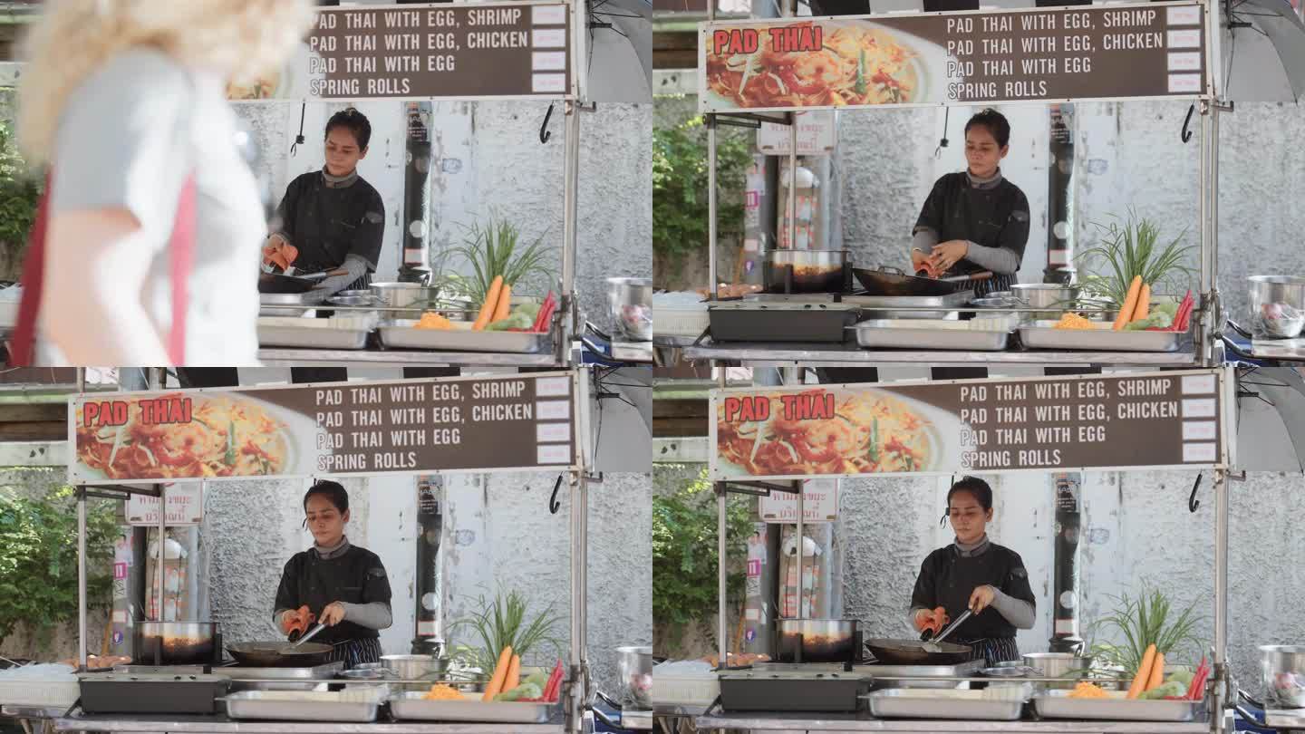 在泰国老城的一个街市上，一个自信的女人在炒锅里做泰式炒粉。