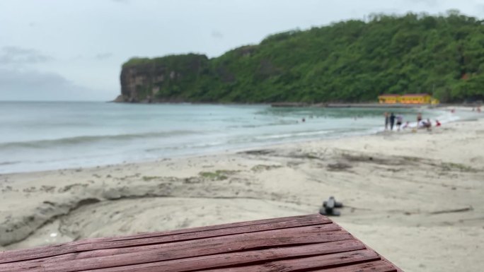 活跃的年轻人喜欢在下雨天漫步在廉价度假海滩的沙滩上。竹桌遮住了视线。模糊了