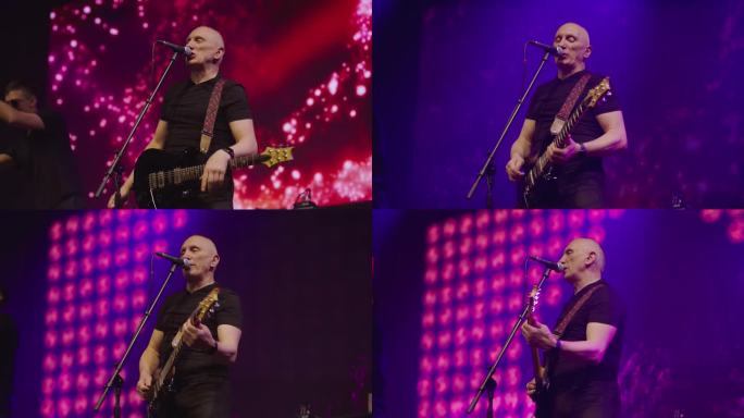 在流行乐队的演出中，贝斯吉他手在舞台上对着麦克风唱歌。舞台由蓝、粉红和红色的灯光照亮