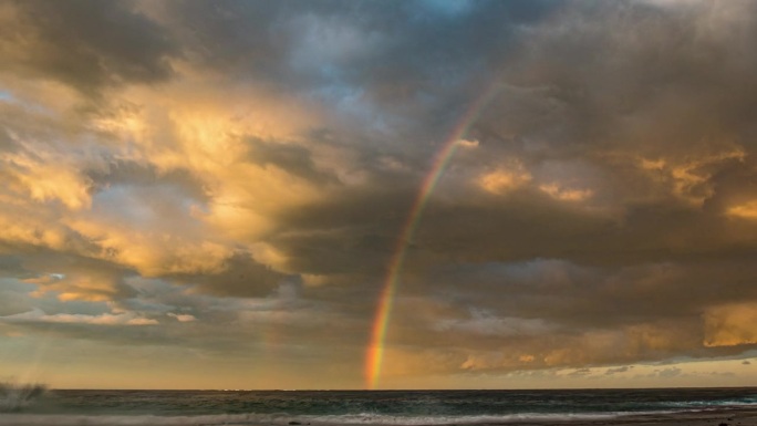 延时拍摄的戏剧性风暴云在日落时在海洋上移动，形成明亮的彩虹