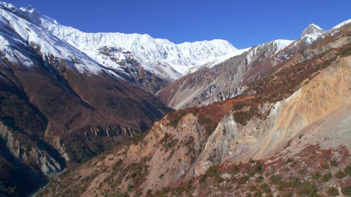 阳光明媚的日子里，喜马拉雅山脉的风景。深谷环绕着岩石斜坡和积雪山脊。马南山谷，安纳普尔纳环行，尼泊尔