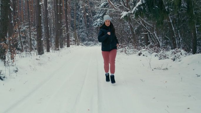 冬季运动。一名生活方式积极的妇女在白色的冬季森林中慢跑