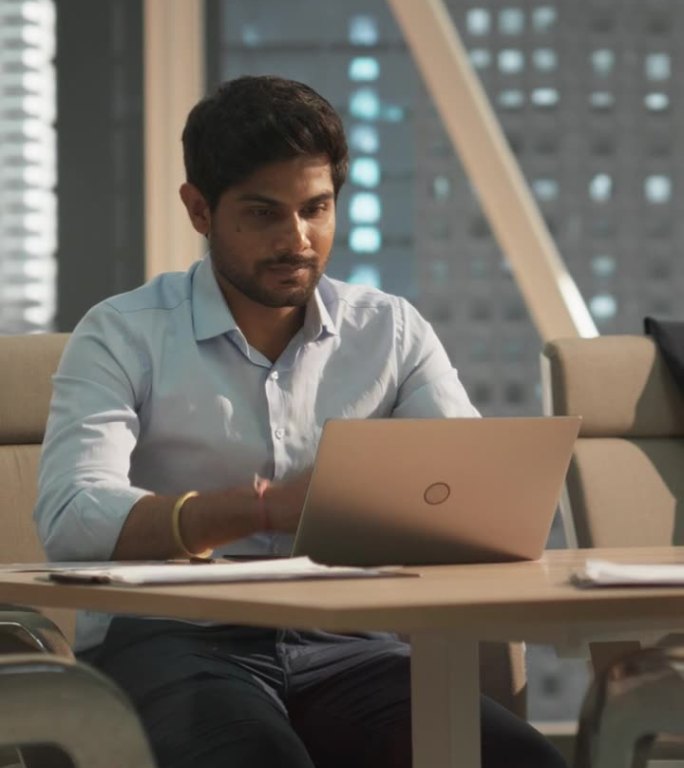 垂直屏幕:年轻的印度客户经理在现代公司办公室的笔记本电脑上工作。处理财务报告，为公司准备增长计划