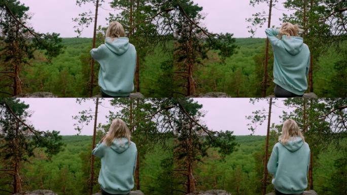 身穿淡蓝色薄荷运动衫的金发女子的后视图，对面是森林。