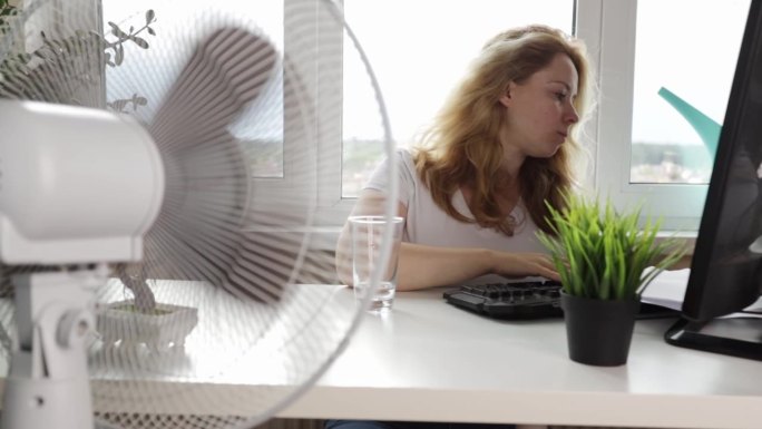 女人在夏天用风扇在办公室里流通空气，夏天在室内发暑
