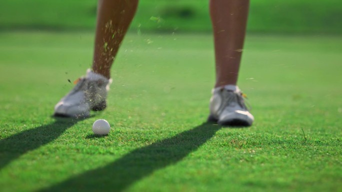 女子腿在草地球场打高尔夫球。高尔夫球手在室外击球。