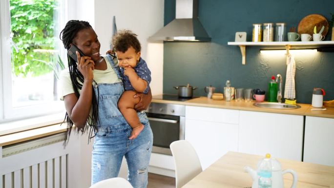 黑人母亲抱着儿子在厨房打电话
